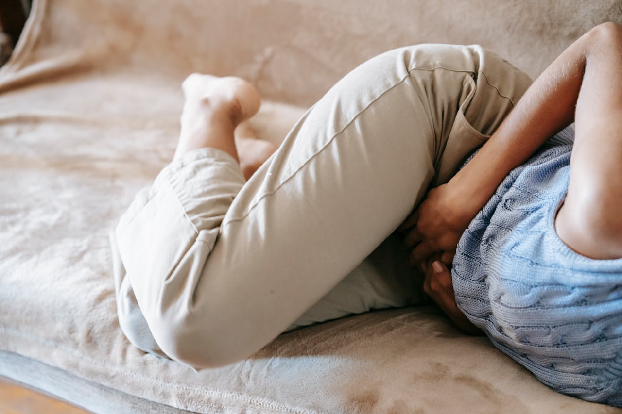 A person in pain holding their stomach while lying on a couch indoors, suggesting discomfort or illness.