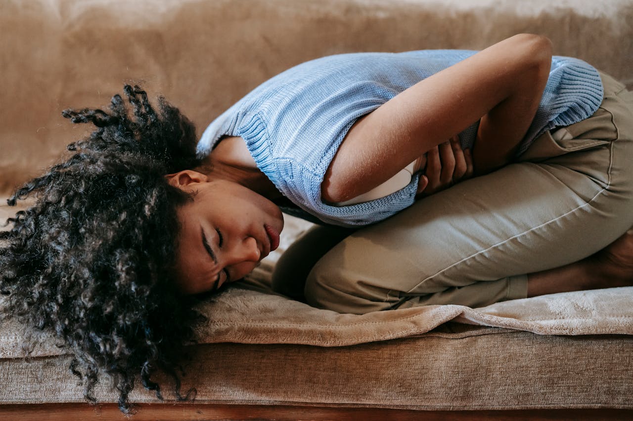 Home Side view of young African American female in agony on couch while having pain in stomach